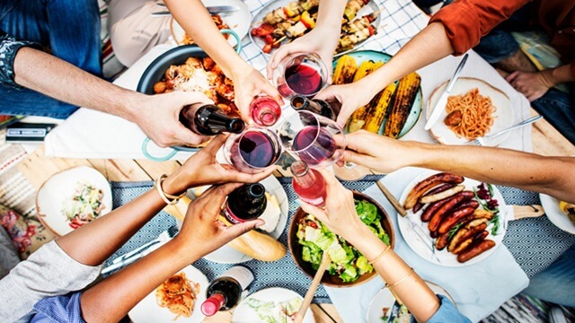 People toasting with wine glasses over a table filled with assorted foods